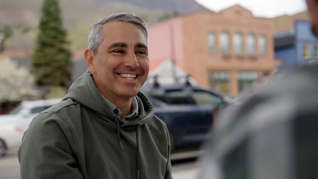 Alex Kelloff smiling in a green jacket on a downtown Aspen street