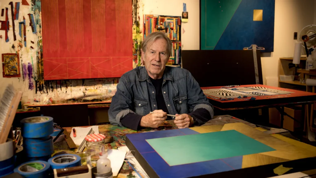 Artist Richard Carter seated in his studio surrounded by colorful geometric paintings