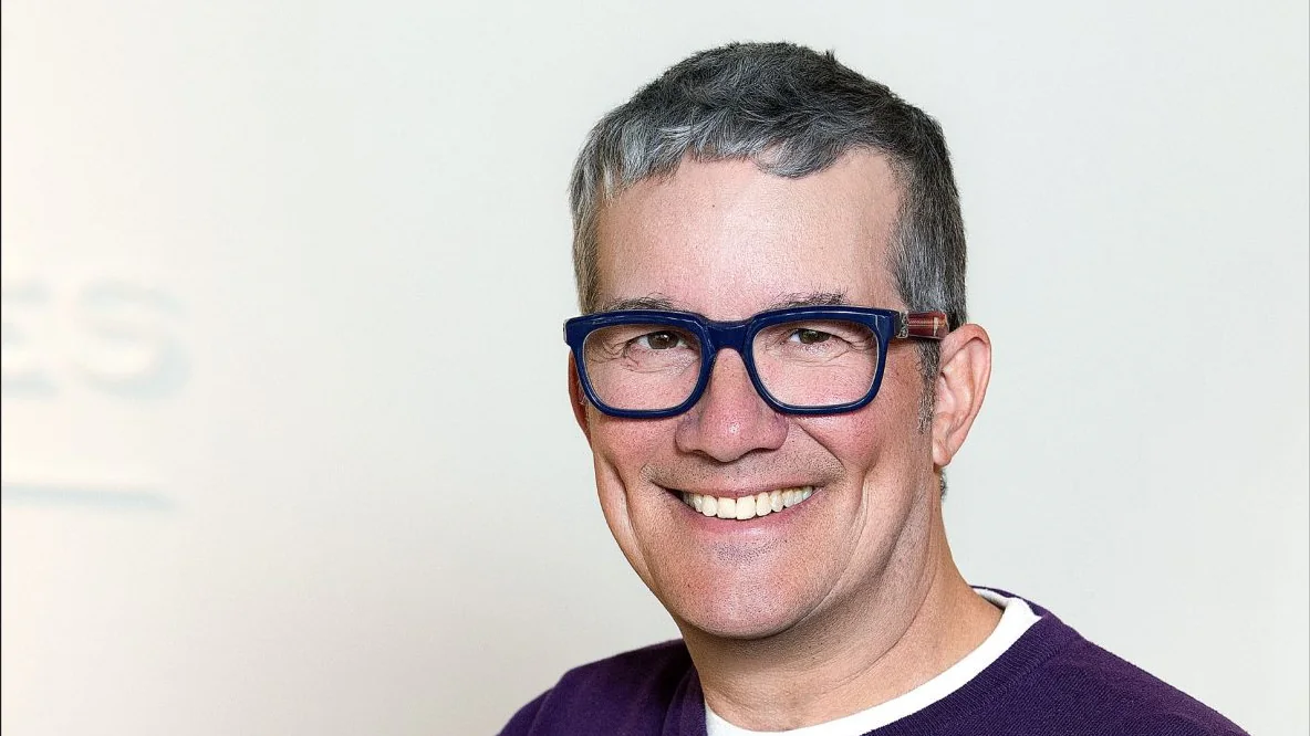 Scott Poupore, Aspen optical business owner, smiling in blue glasses and a purple sweater